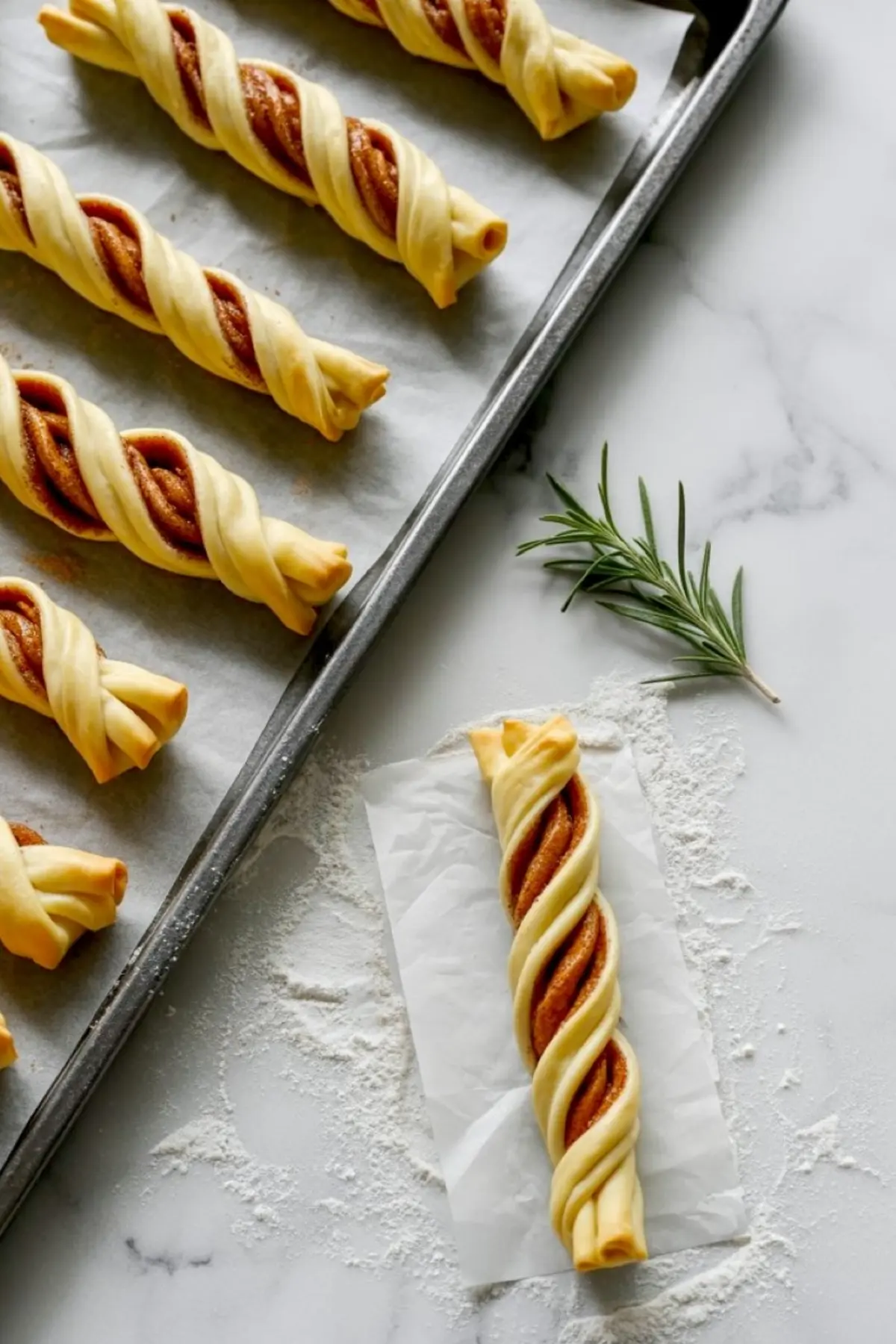 Unbaked puff pastry cinnamon twists arranged on a parchment-lined baking tray, filled with cinnamon sugar and shaped in a spiral twist ready for the oven.