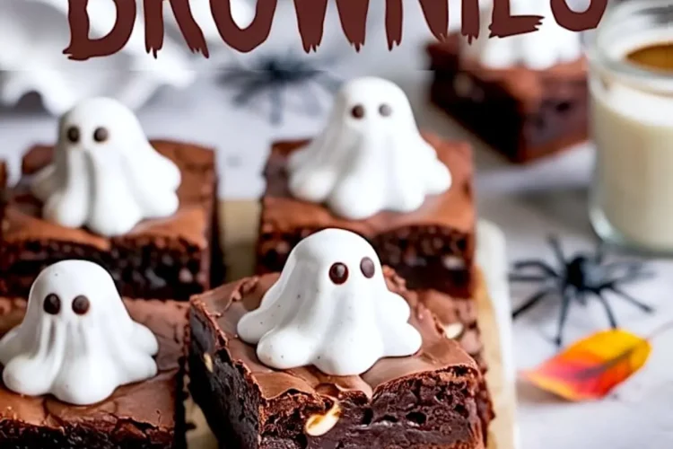 Ghost-themed Halloween brownies on a tray, each square topped with a piped white ghost made of meringue and chocolate chip eyes, styled with black spider decorations and a glass of milk.