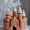 Gingerbread castle decorated with powdered sugar, white icing, colorful candy dots, and striped candy cane arches, displayed on a marble background with winter holiday theme.