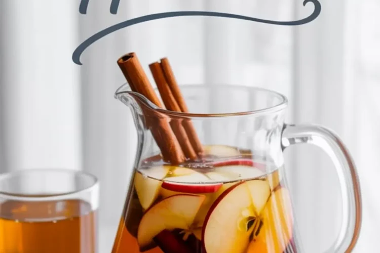 Pitcher of apple cider filled with cinnamon sticks and sliced red apples, surrounded by glasses of cider and the text “homemade apple cider” over a white curtain background.