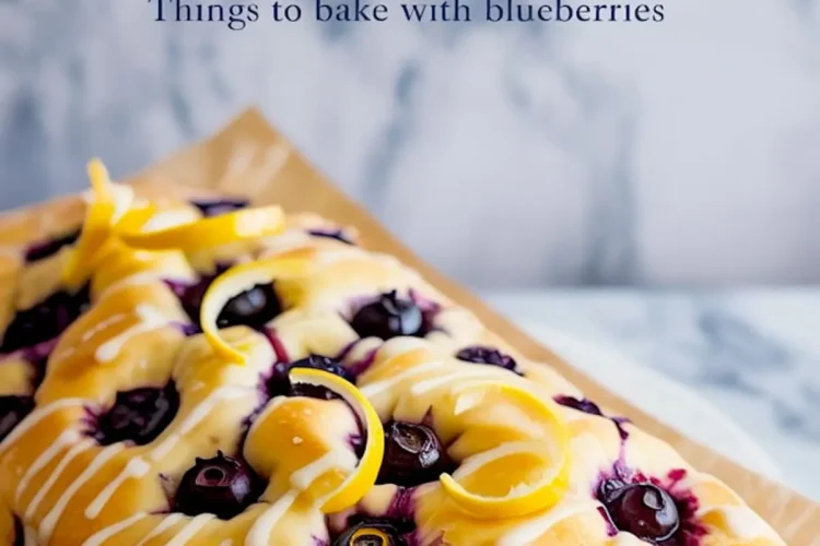Three-quarter view of baked lemon blueberry focaccia loaf with glossy blueberries, white glaze, and curled lemon zest on parchment-lined marble surface.