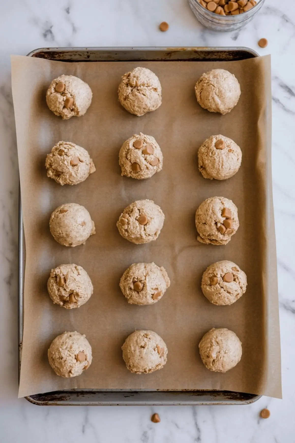 Scooped oatmeal butterscotch cookie dough balls placed in even rows on a parchment-lined baking sheet, ready to be baked.
