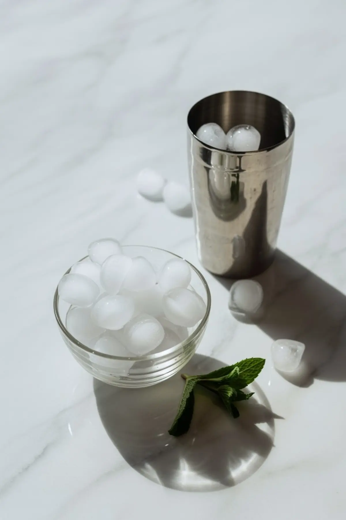 Cocktail shaker surrounded by margarita ingredients including lime, pomegranate, orange juice, pomegranate juice, and measuring tools on a bright marble counter.