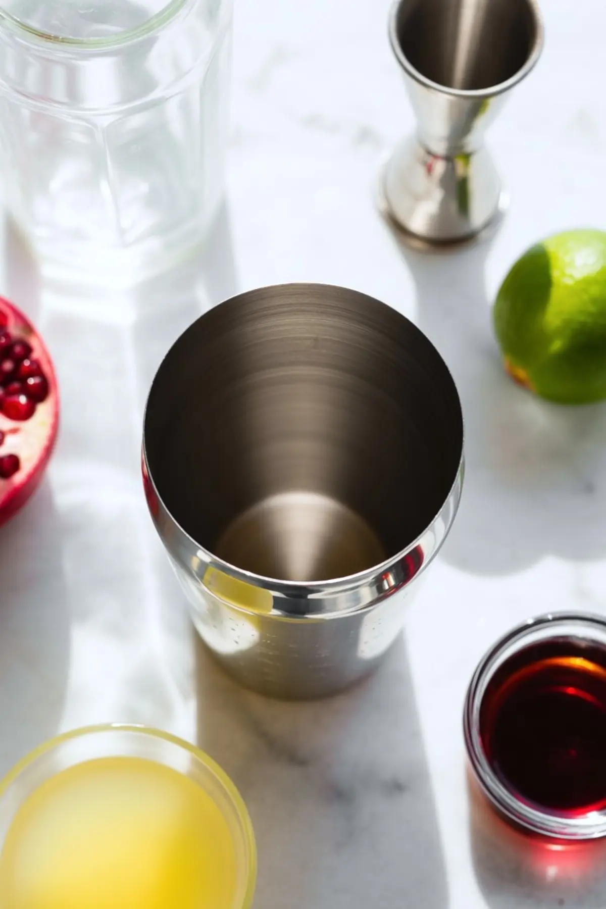 Overhead view of a pomegranate margarita in a salt-rimmed glass, with visible pomegranate seeds and ice cubes, set on a marble background with a nearby lime wedge.