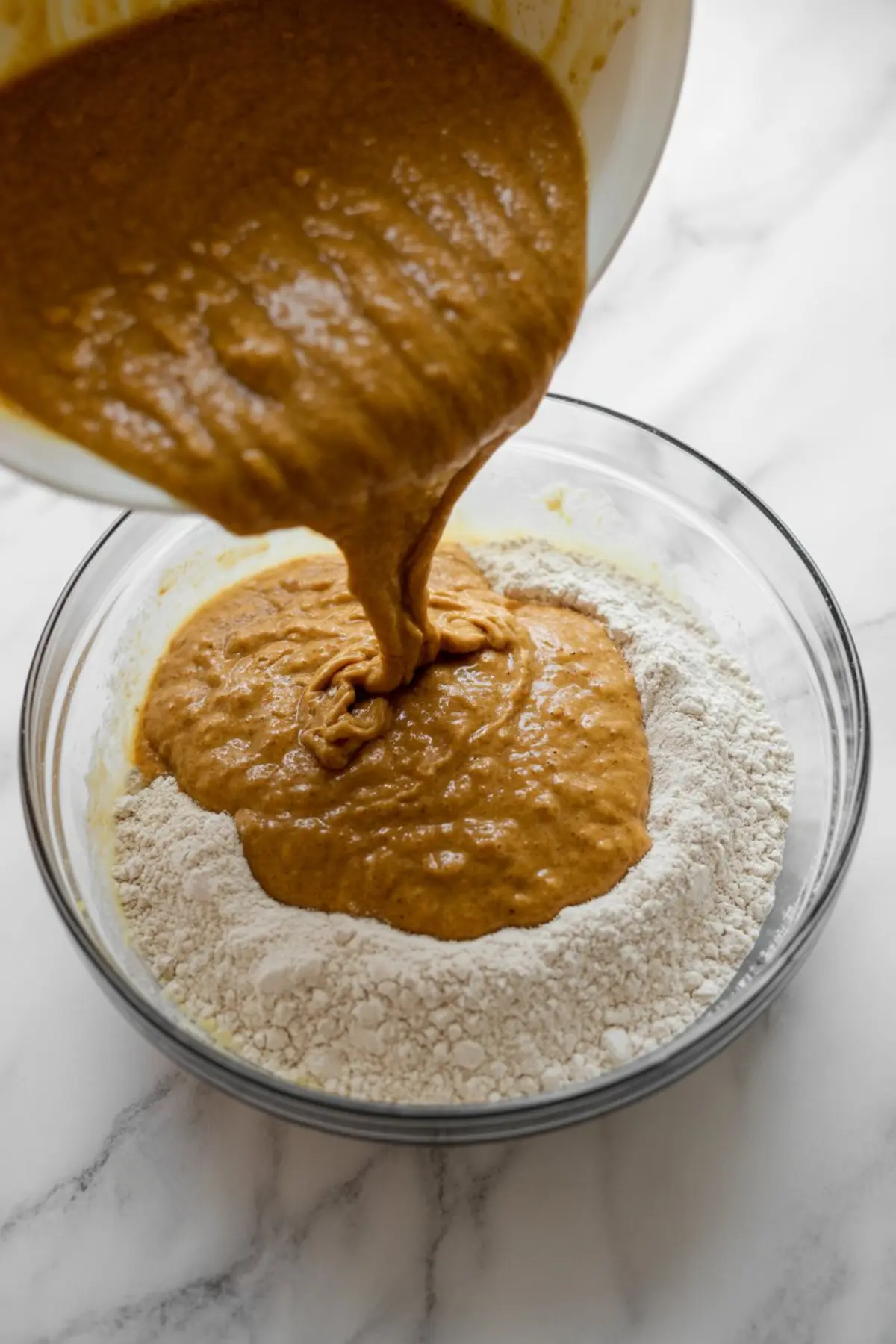 Pumpkin puree being poured into a bowl of dry ingredients, capturing the process of combining wet and dry mix.