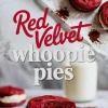 A plate displays red velvet whoopie pies filled with creamy vanilla frosting, with one cut in half to show the fluffy texture and filling, set next to a glass of milk.