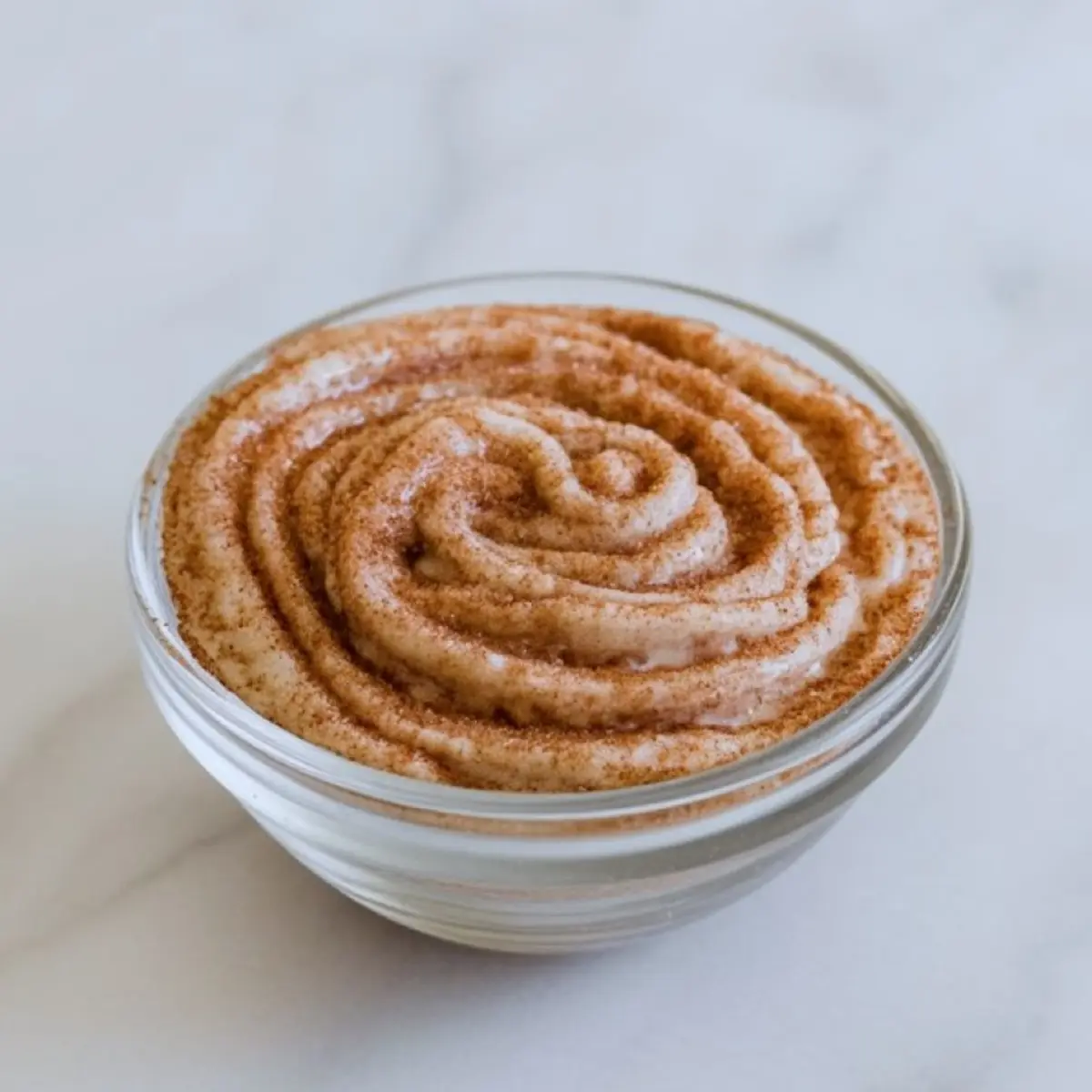 Small glass bowl filled with cinnamon sugar swirl mixture for snickerdoodle banana bread, swirled into a thick, creamy texture and dusted with ground cinnamon.
