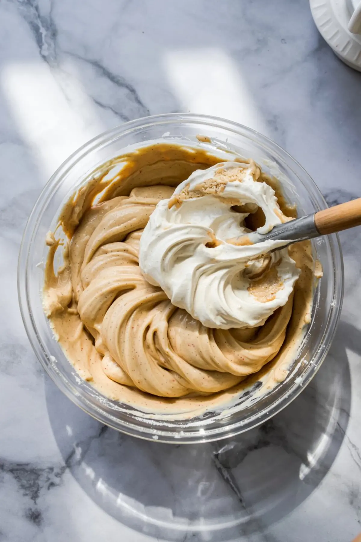 Partially mixed peanut butter and whipped topping in a glass bowl with spatula, showing swirled creamy texture for dessert dip base.
