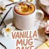 Vanilla mug cake with a bite on a spoon above the mug, showing moist crumb texture, surrounded by vanilla pods, white chocolate, and flowers on a marble surface.