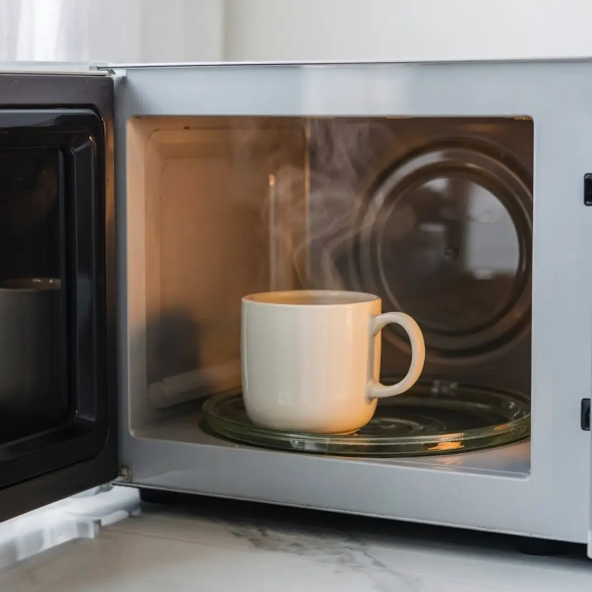White mug with steam rising inside a microwave, showing the vanilla mug cake heating process during microwave baking.
