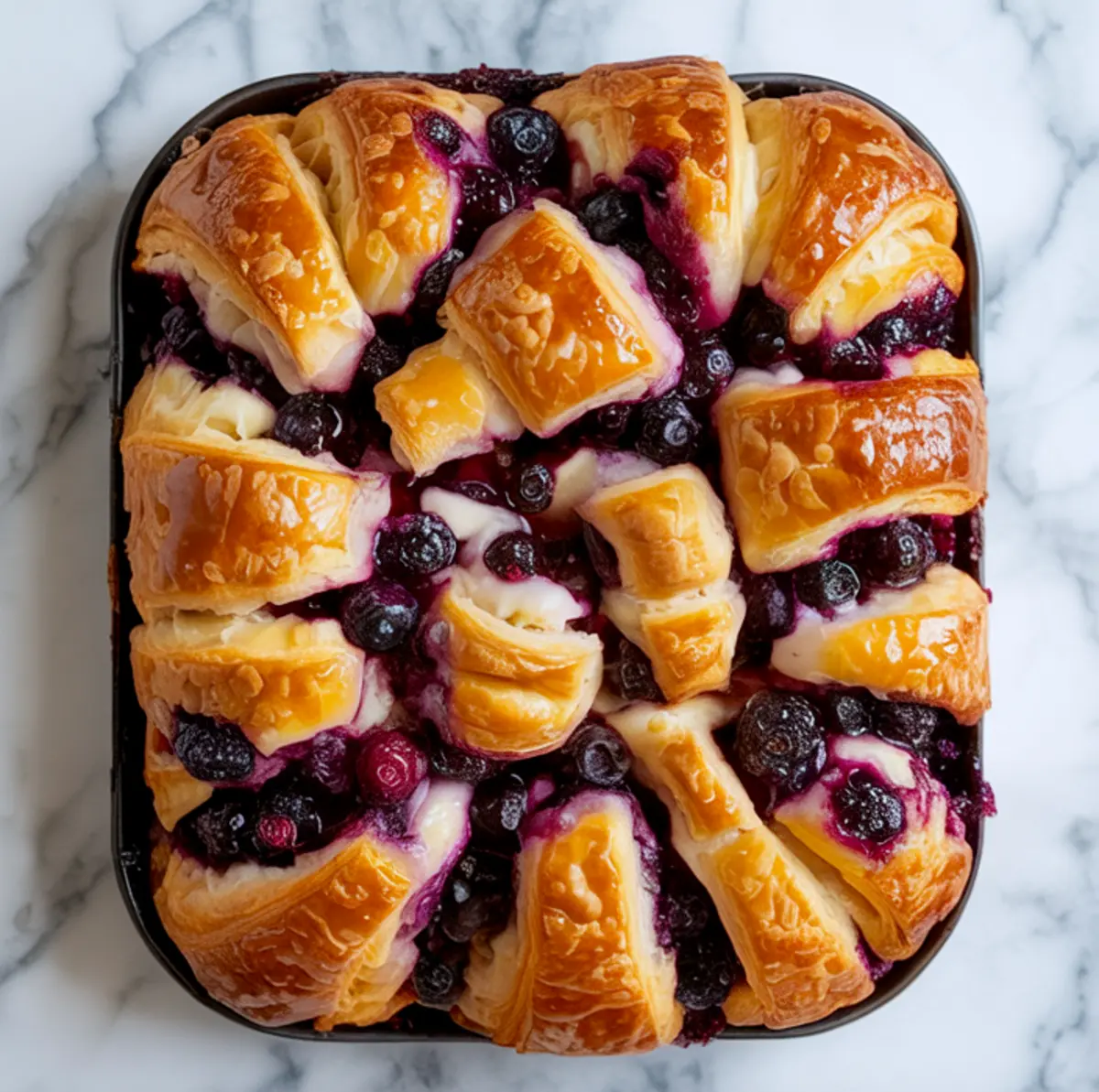 Close-up top-down view of blueberry cream cheese croissant casserole baked with golden croissant pieces and bursting blueberries in a creamy custard base.