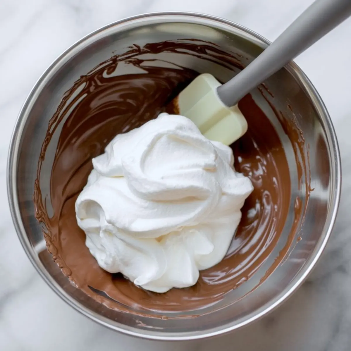 Stainless steel bowl with whipped cream added to melted chocolate, ready for folding into chocolate mousse mixture.