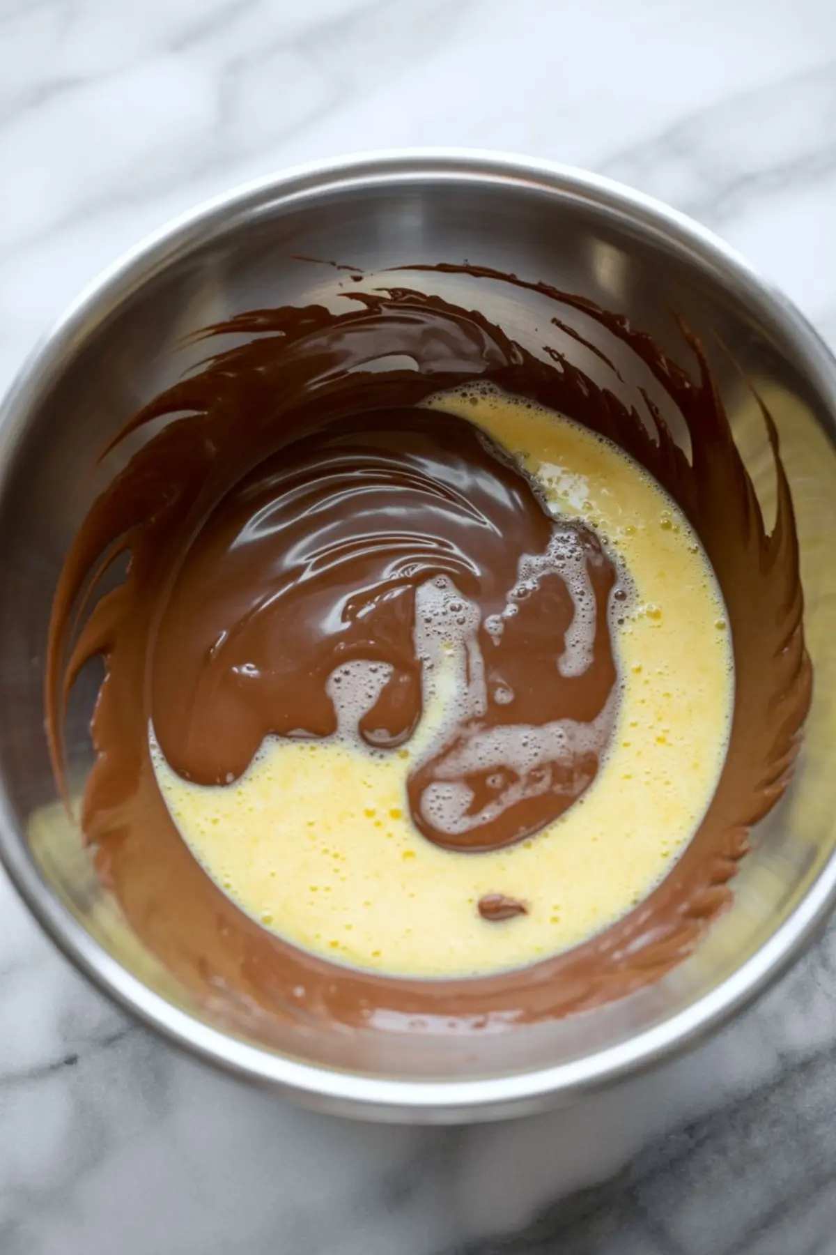 Melted chocolate combined with an egg mixture in a metal bowl, showing the early stage of chocolate mousse preparation.