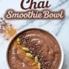 Chocolate chai smoothie bowl topped with cardamom pods, chocolate bits, and a line of ground cinnamon, with a background of scattered cinnamon powder and text overlay.