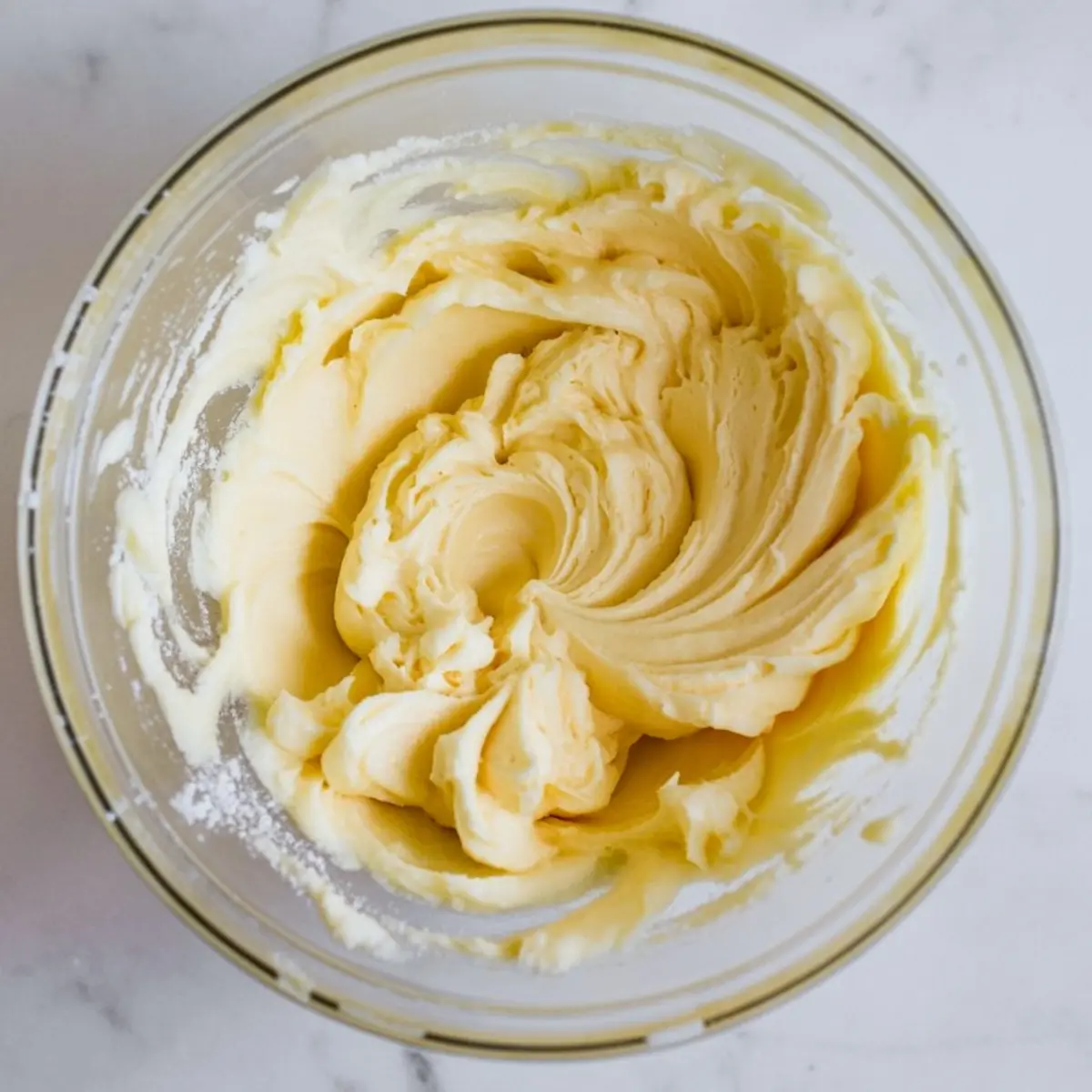 Whipped butter and sugar mixture in a glass bowl, showing a smooth and creamy texture, ideal for cake or cookie batter preparation.