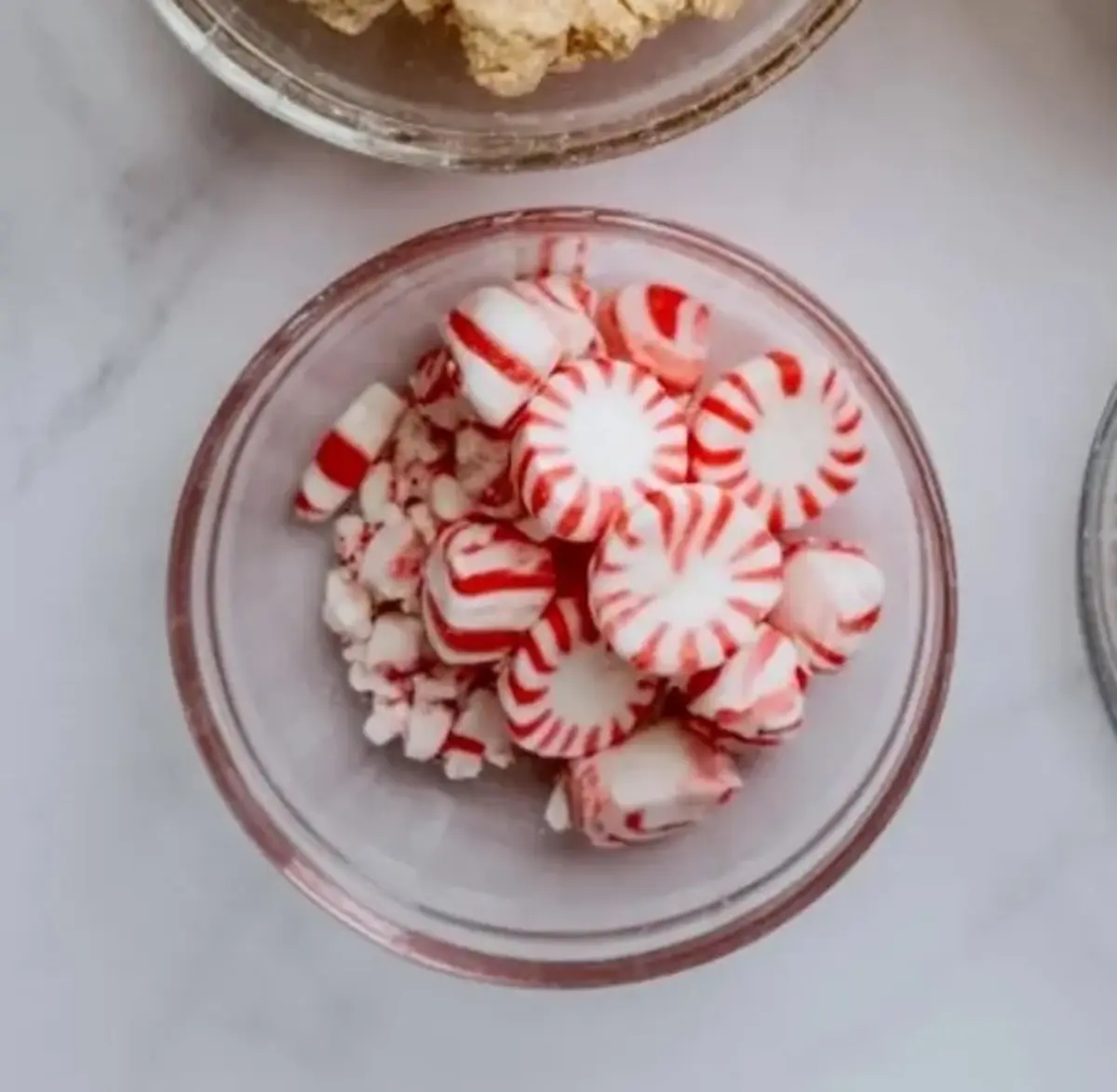 Clear glass bowl holds whole and crushed red-and-white peppermint candies for Christmas crumble cookie garnish.
