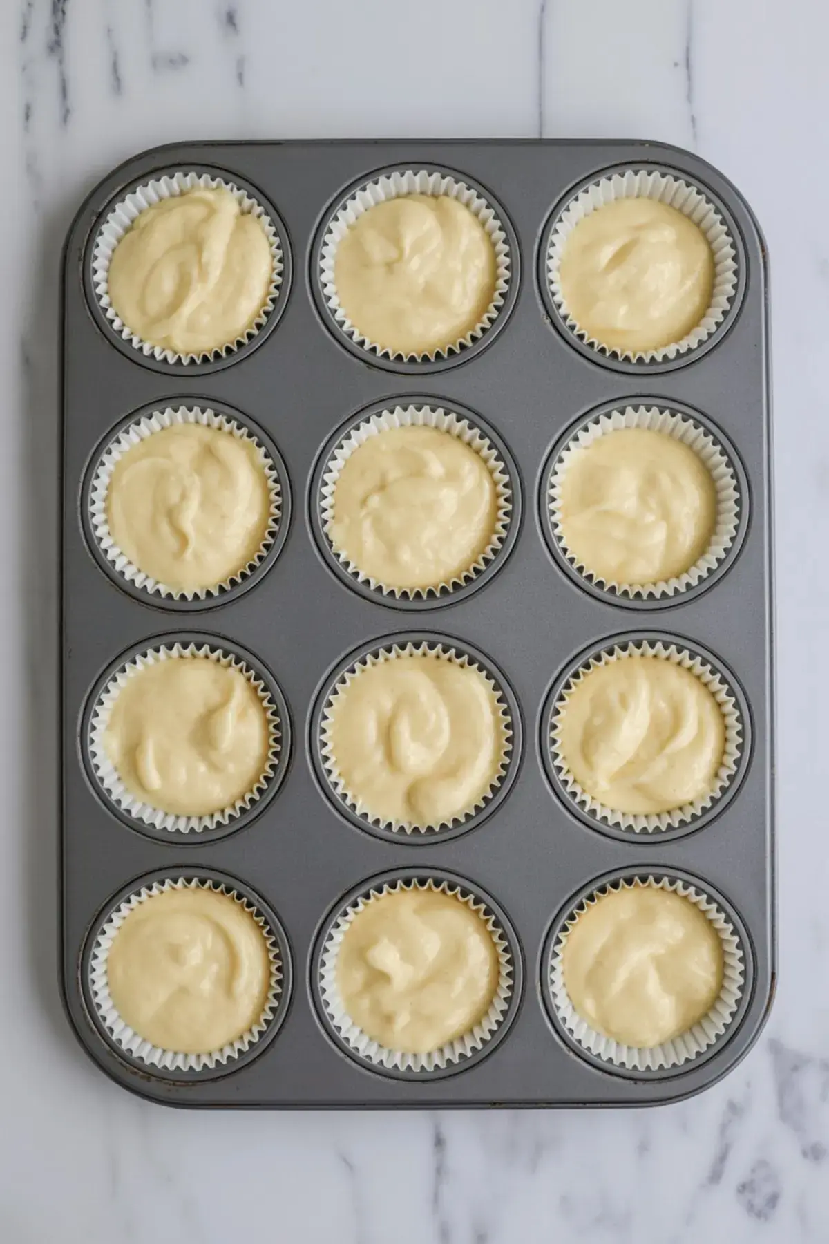 Cupcake tray filled with pale yellow cake batter in white liners, ready to be baked. A great step-by-step photo for easy cupcake recipes or cake preparation tutorials.
