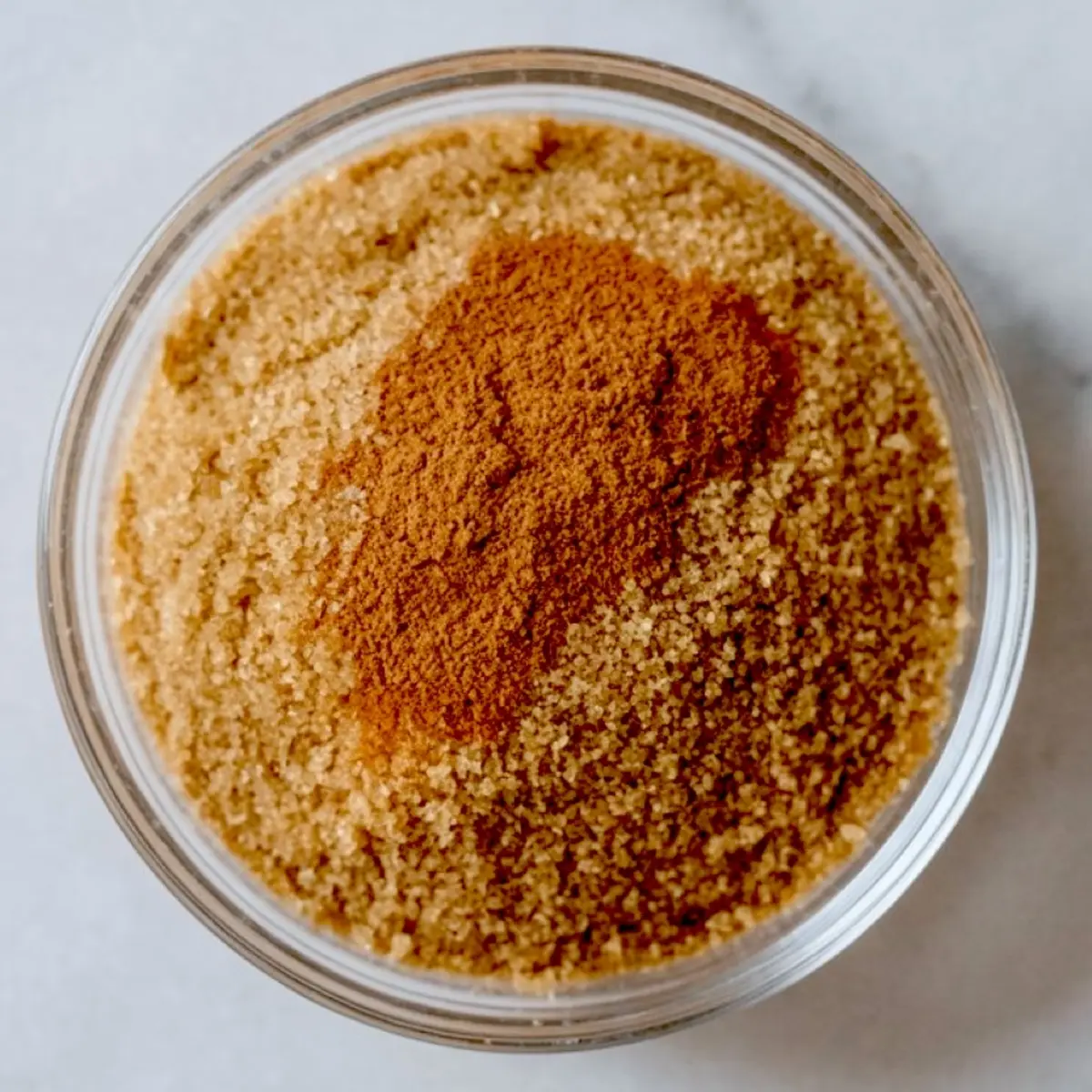 Close-up of a glass bowl filled with brown sugar and cinnamon, showing the spice blend used for topping Christmas dump cake recipes.