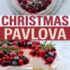 Overhead and side view of a Christmas pavlova covered with raspberries, blueberries, blackberries, and cranberries dusted with powdered sugar and rosemary. Lower half shows the pavlova slice with thick meringue layers and dripping red berry sauce.