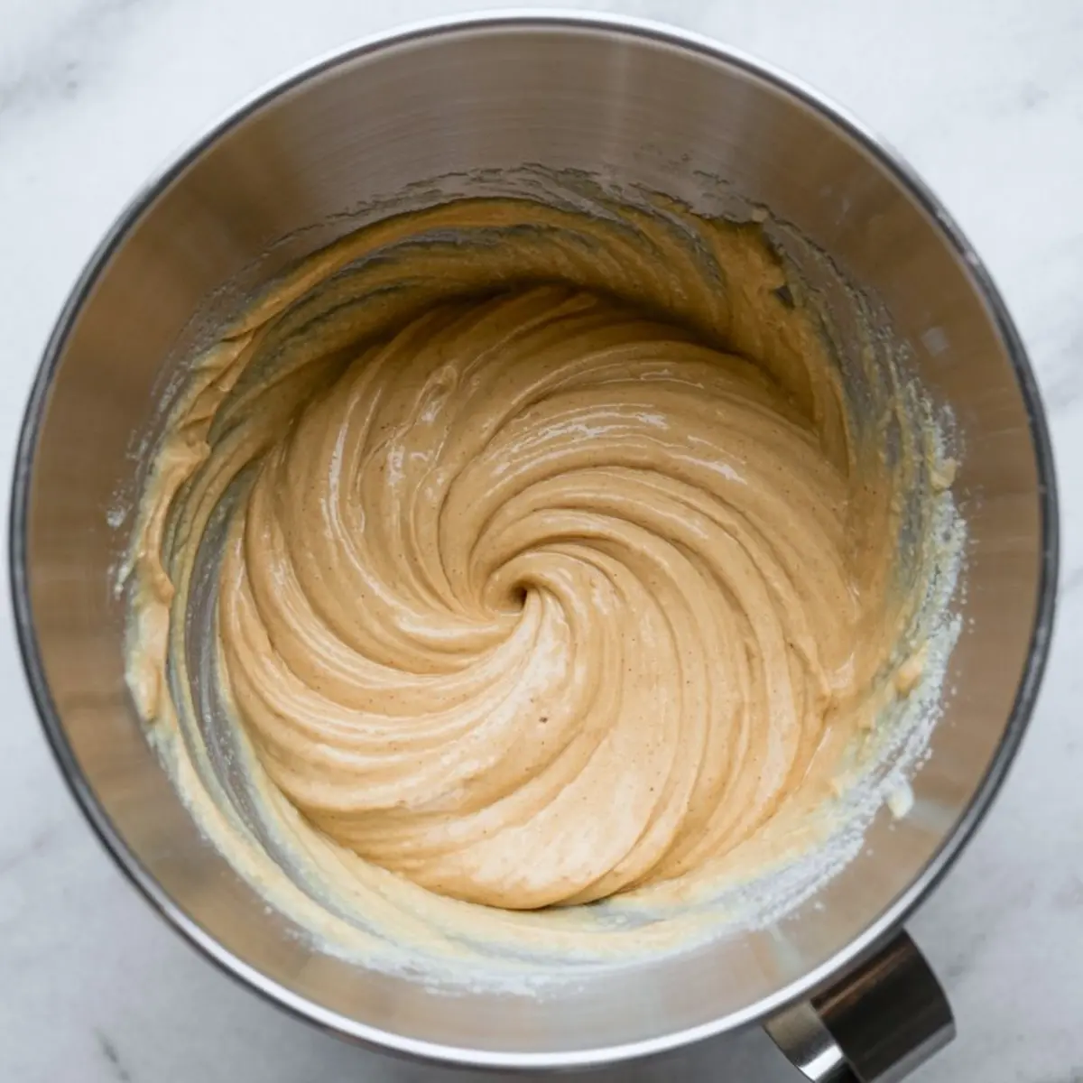 Creamy spiced cheesecake batter swirled in a stainless steel mixing bowl, showcasing a smooth and thick consistency.
