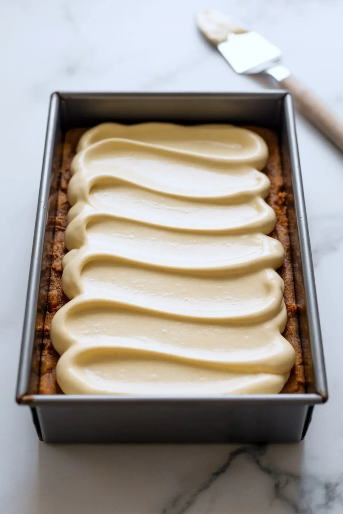 Rectangular baking pan filled with gingerbread cheesecake batter spread evenly over a baked gingersnap crust.
