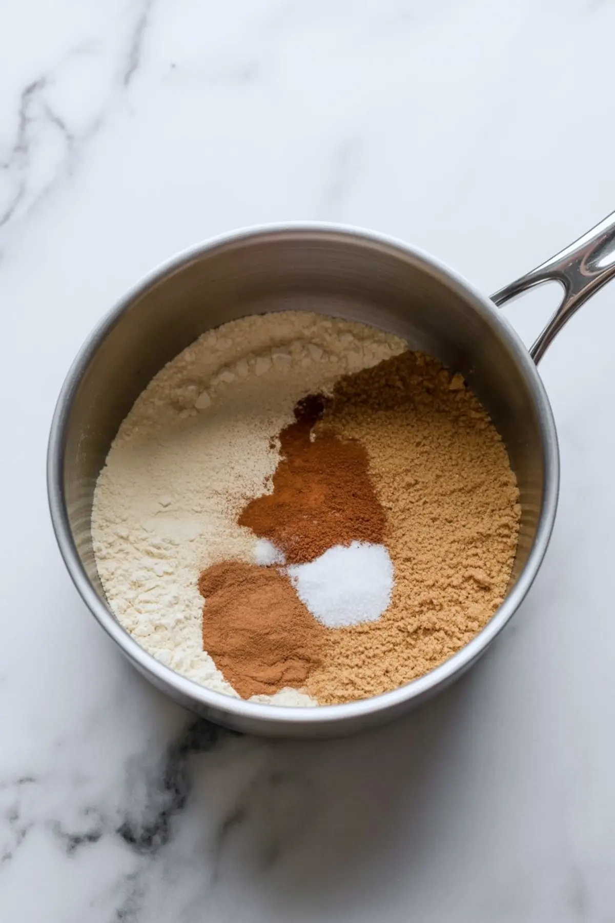 Stainless steel saucepan with dry ingredients for gingerbread pudding, including flour, ground cinnamon, ginger, salt, and brown sugar.
