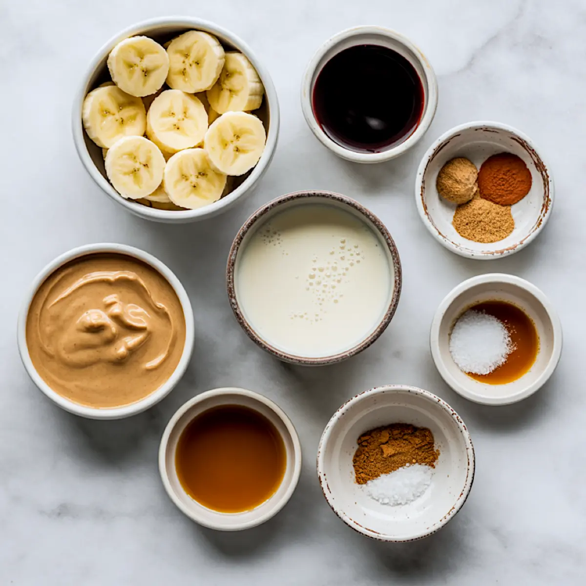 Overhead flat lay shows small bowls of banana slices, dark molasses, almond milk, nut butter, maple syrup, vanilla, ground ginger, cinnamon, and sea salt arranged for a gingerbread smoothie bowl recipe.