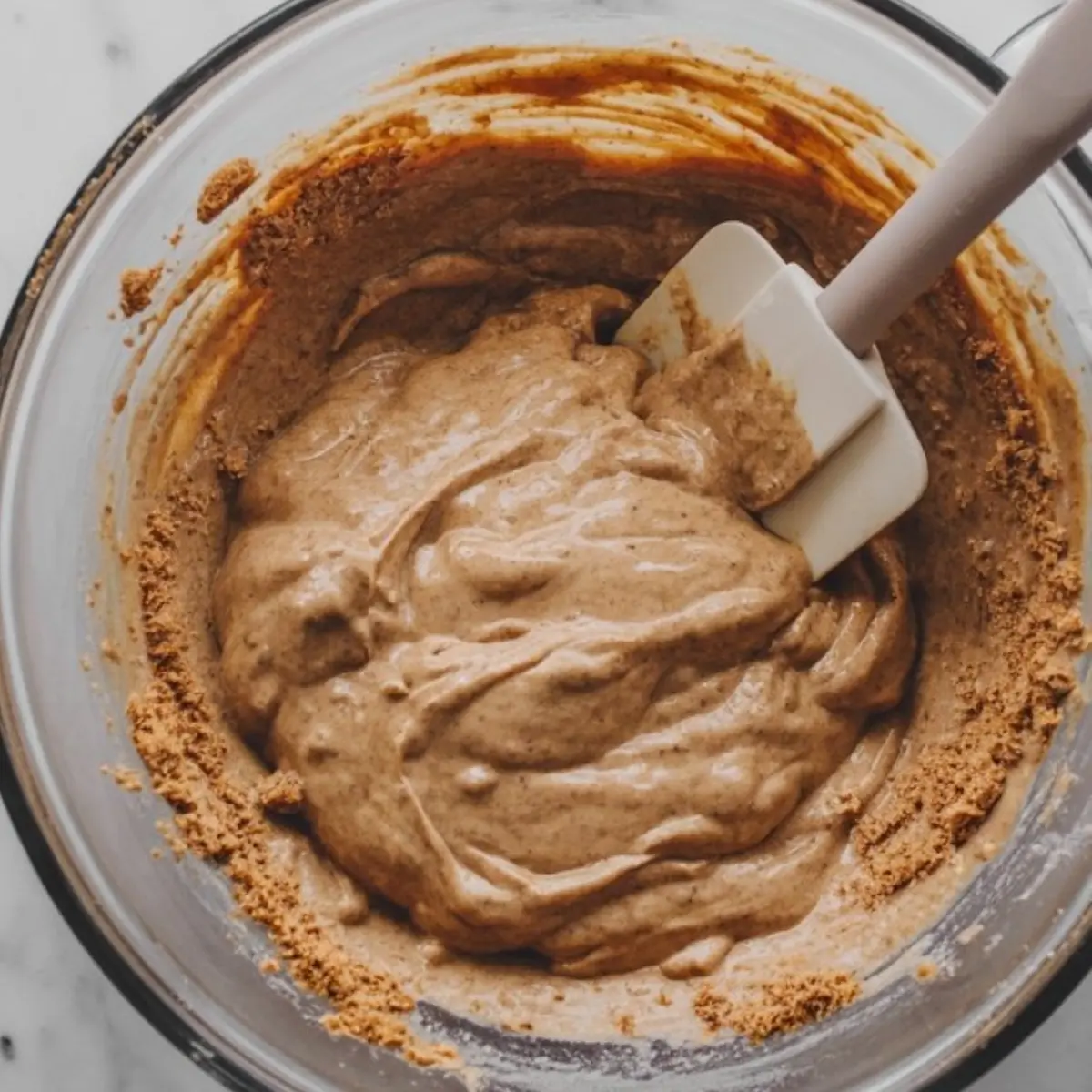 Mixing bowl filled with gingerbread truffle dough being stirred with a white silicone spatula, with crushed cookie crumbs clinging to the sides.
