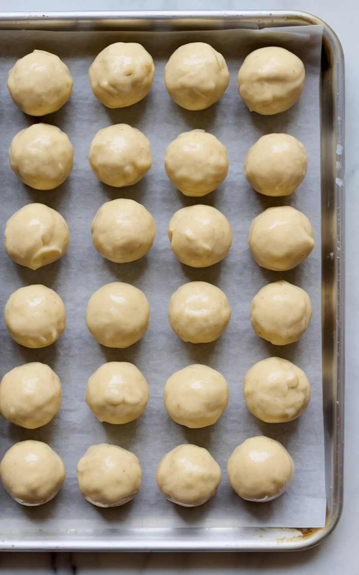 Baking tray lined with parchment paper holding uniform rows of gingerbread truffle balls coated in white chocolate before decorating.
