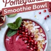 Holiday pomegranate smoothie bowl with a rich red base topped with glossy pomegranate seeds, toasted coconut flakes, and fresh mint, displayed under a tilted recipe title.