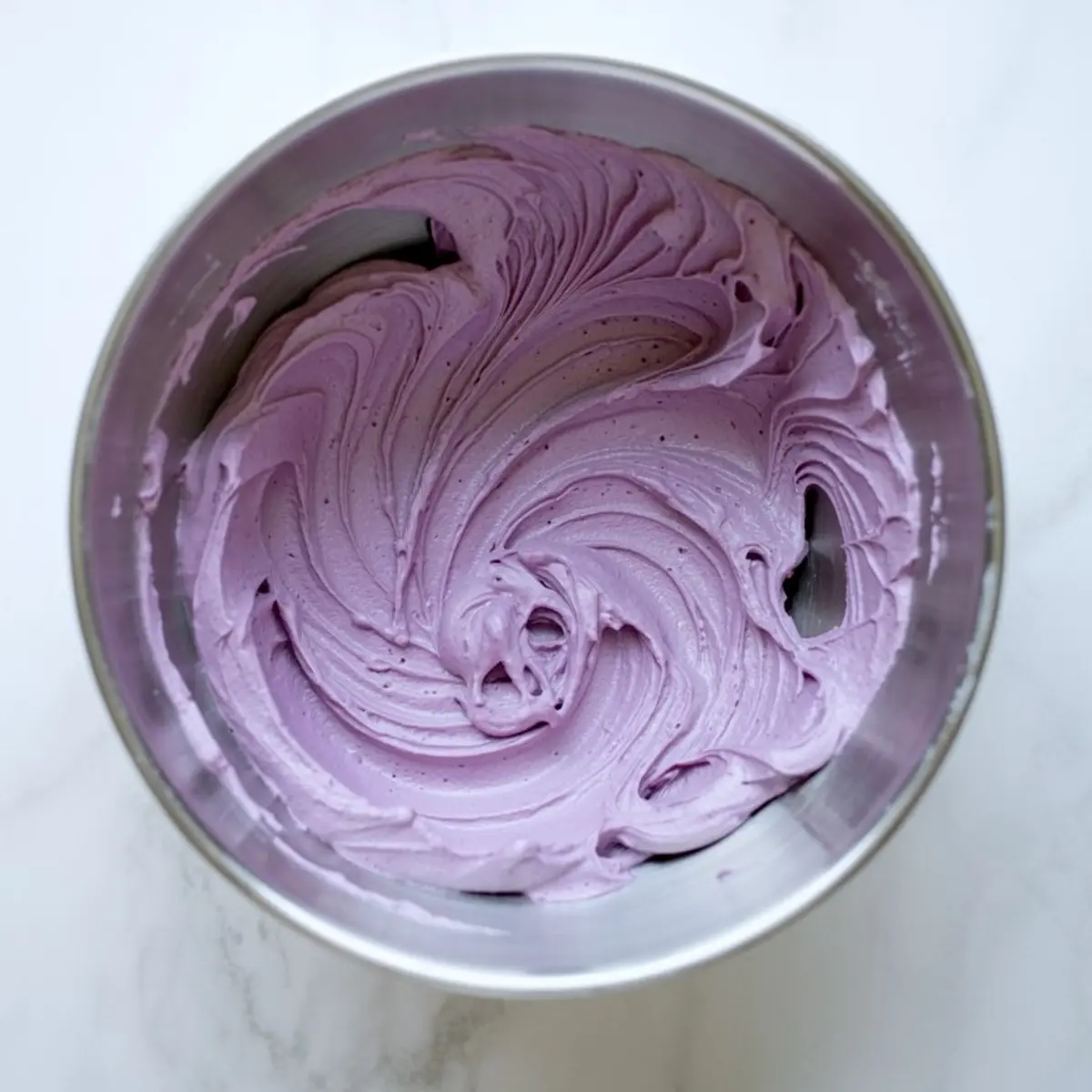 Purple buttercream frosting swirled in a stainless steel mixing bowl, showing a smooth and creamy texture ideal for decorating cupcakes or cakes.