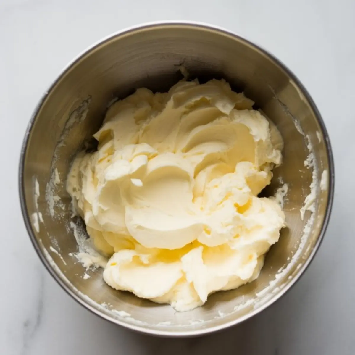 Fluffy buttercream frosting with a pale yellow tint in a metal bowl, ready for flavoring or piping.