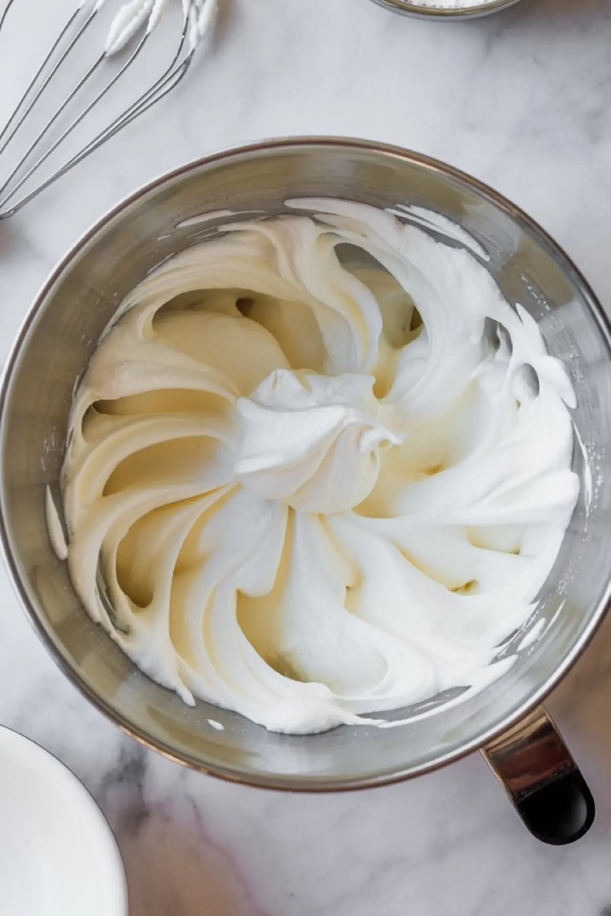 Freshly whipped cream in a metal mixing bowl with soft peaks, ready to be layered into peppermint mocha pudding parfaits.
