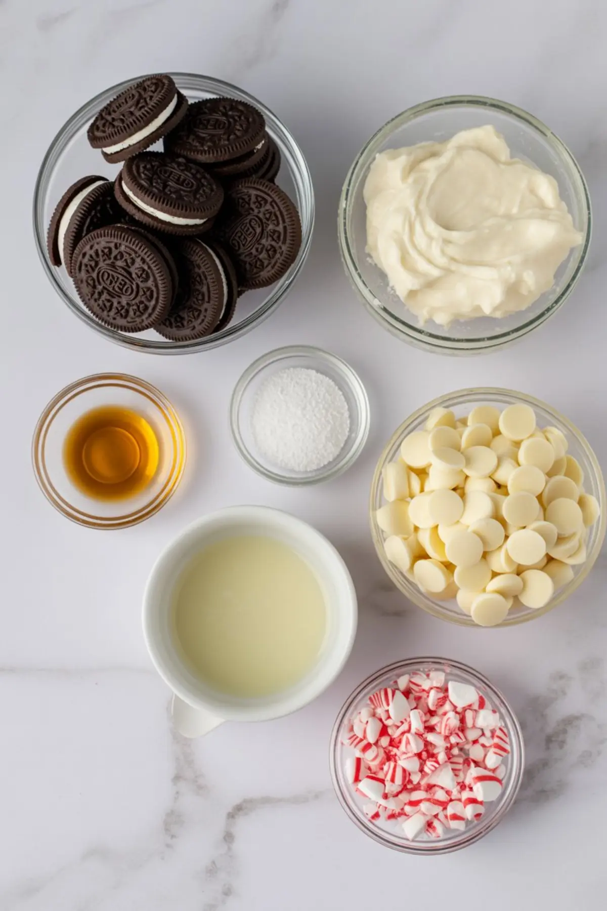 Flat lay of peppermint Oreo truffle ingredients including Oreo cookies, cream cheese, white chocolate chips, crushed peppermint candies, vanilla extract, powdered sugar, and sweetened condensed milk.
