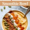 Close-up of a pumpkin pie smoothie bowl topped with pumpkin seeds, granola, Greek yogurt, cinnamon, and a maple drizzle, served with a spoon on a marble surface.