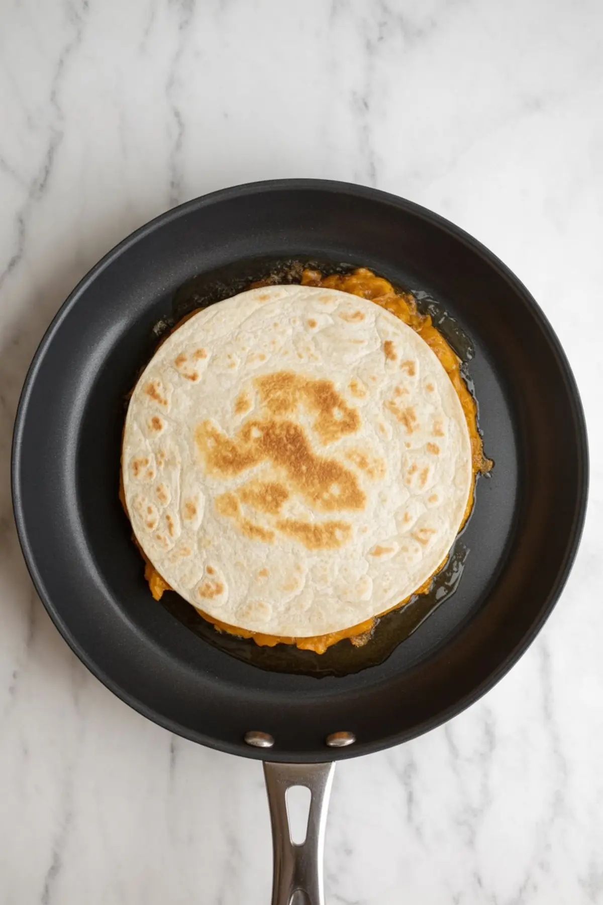 Pumpkin spice quesadilla cooking in a non-stick skillet, with golden toasted flour tortillas and pumpkin filling visible around the edges.
