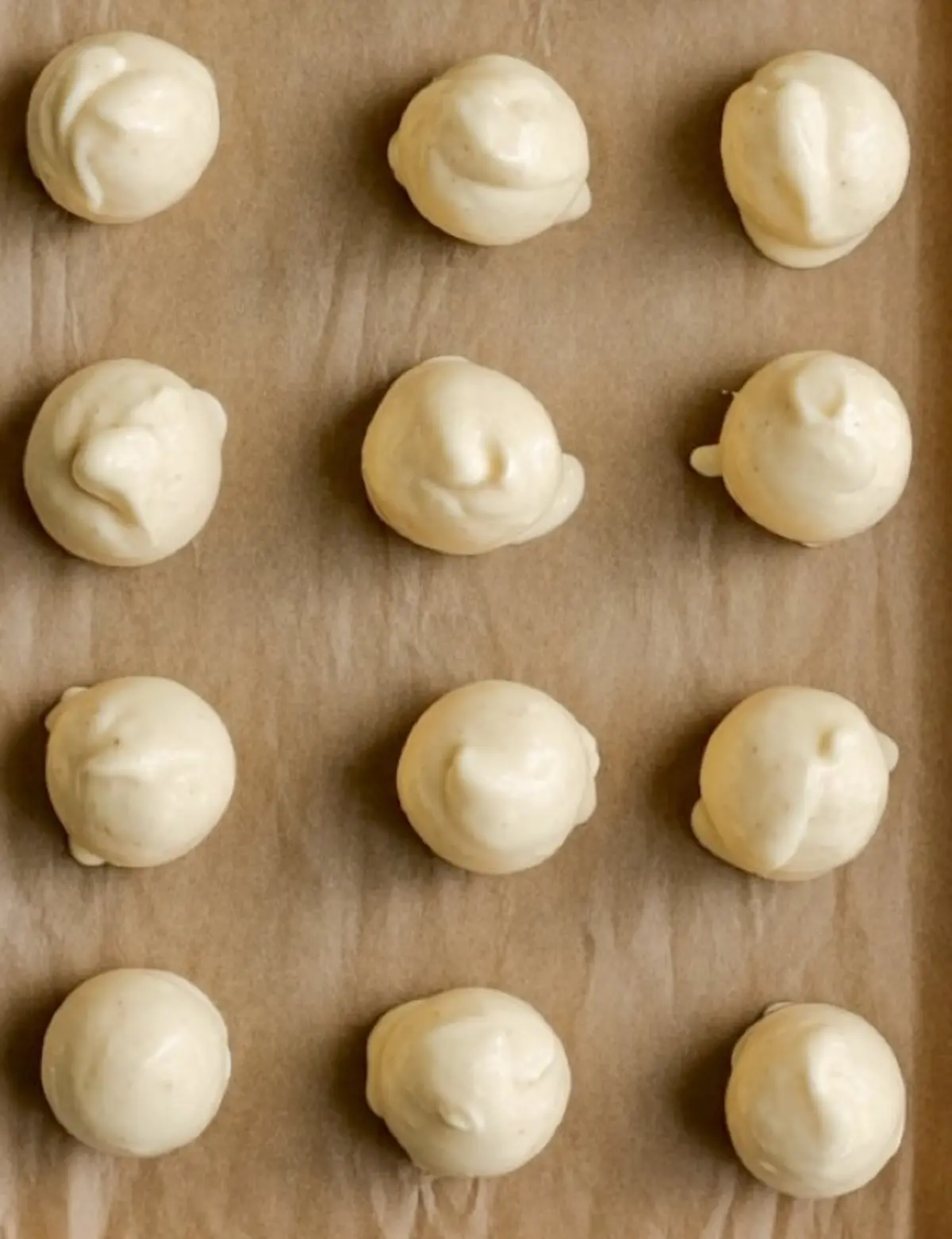 Cream cheese filling scooped into uniform round mounds on a parchment-lined baking sheet, ready to be frozen for red velvet cheesecake cookies.