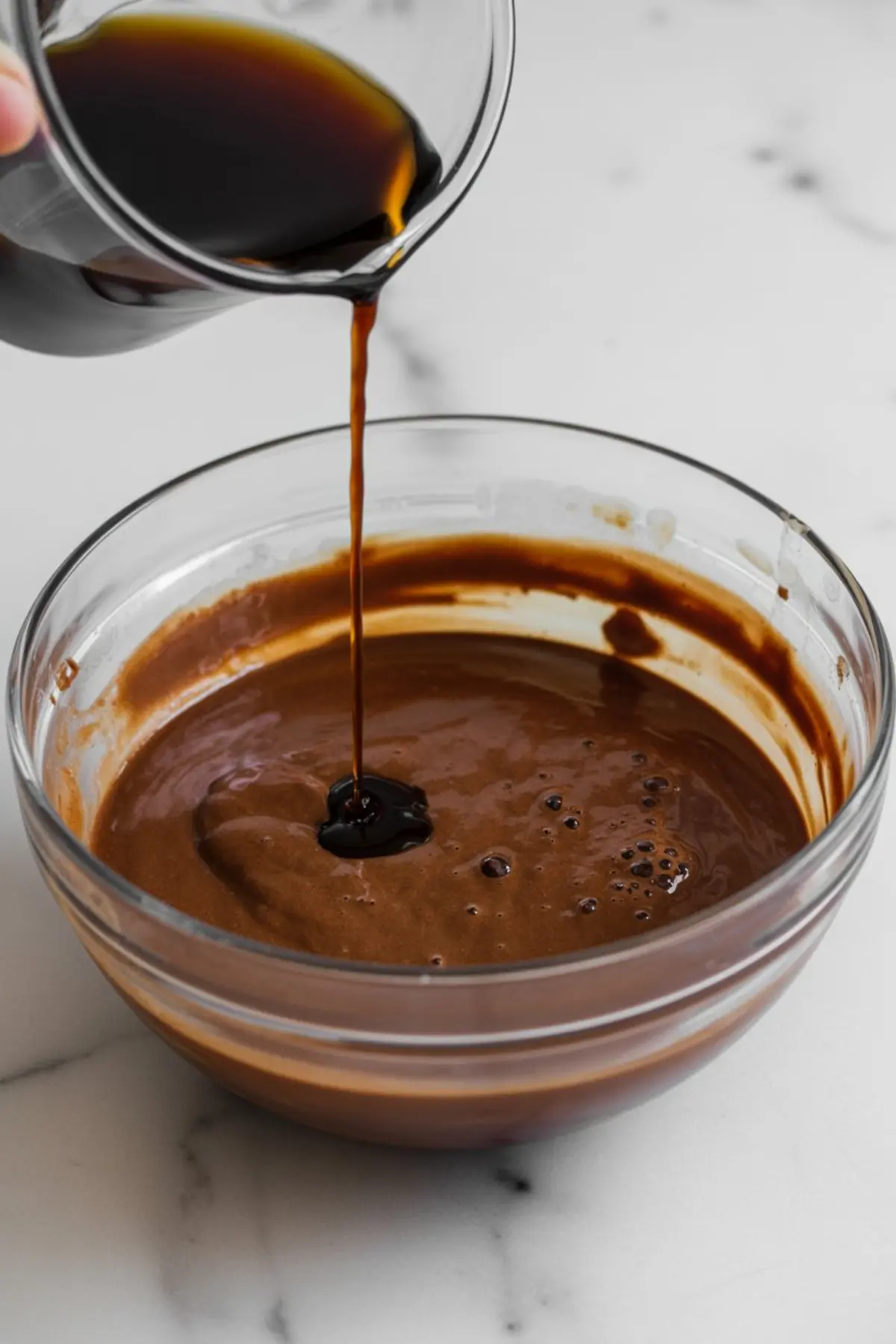 Thick chocolate syrup being poured into a bowl of chocolate batter, creating a rich mixture for a decadent dessert base.