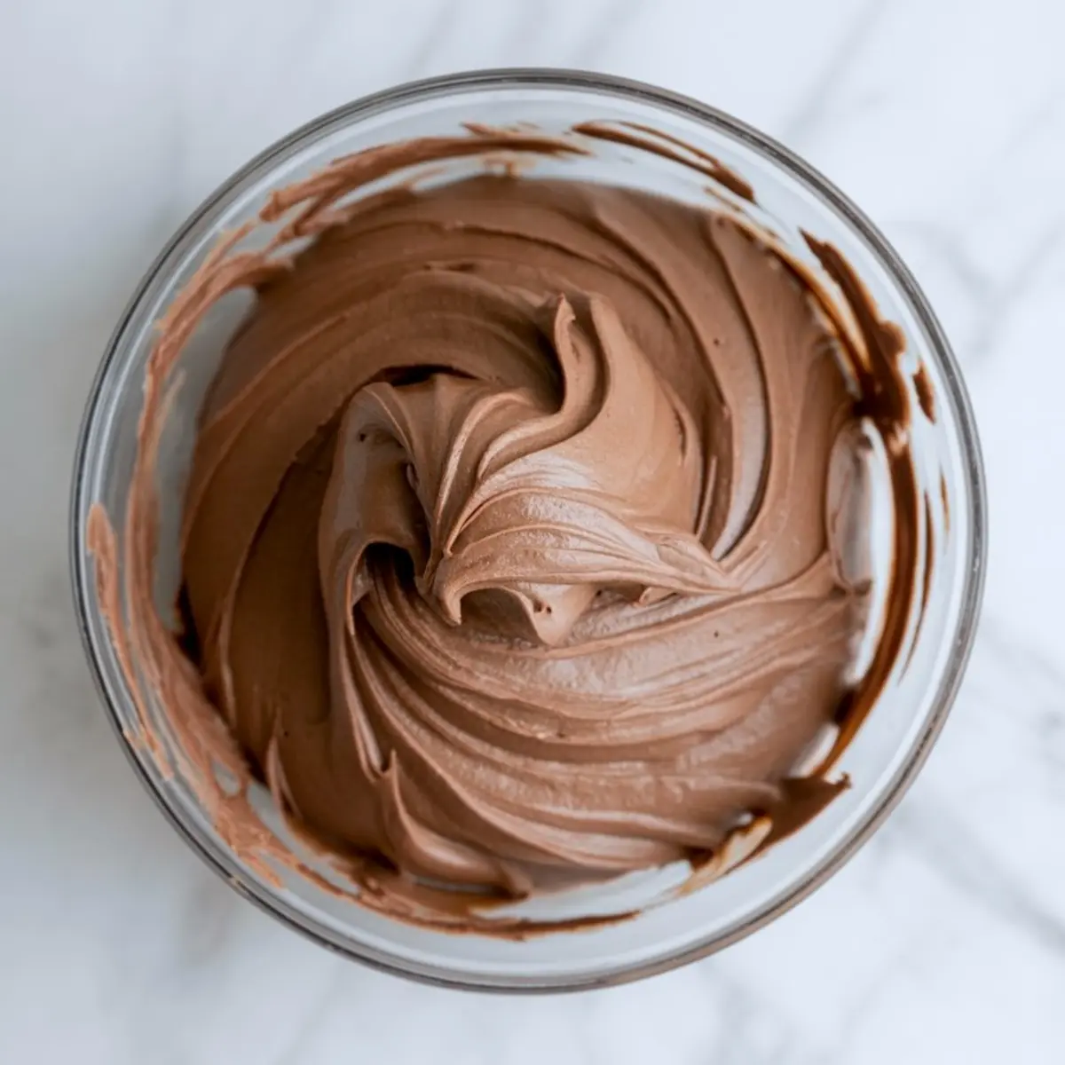 Smooth and swirled chocolate cupcake batter in a glass bowl, whipped to a fluffy consistency, ideal for baking moist chocolate cupcakes.