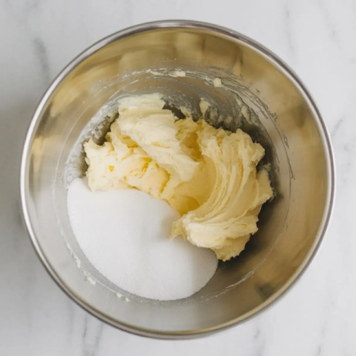 Softened butter and granulated sugar in a metal mixing bowl, ready to be creamed for a holiday cookie recipe.