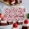 Flat lay and close-up collage of Santa hat brownie skewers made with chocolate brownies, fluffy marshmallows, and ripe strawberries on skewers, styled on parchment paper and a white marble surface with decorative holiday presentation.