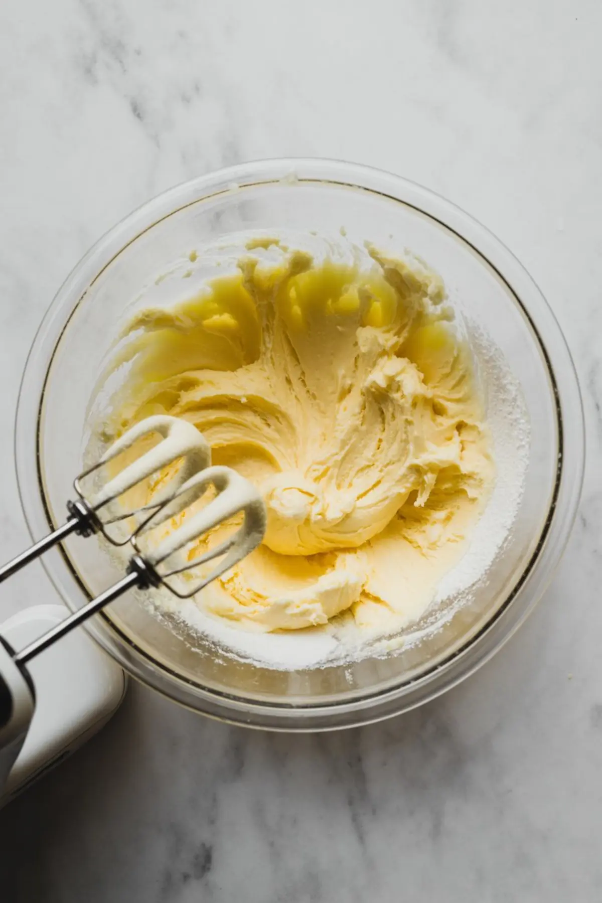 Creamed butter and sugar mixture in a glass bowl with electric beaters resting inside, ready for the next step in the vanilla cake batter preparation.