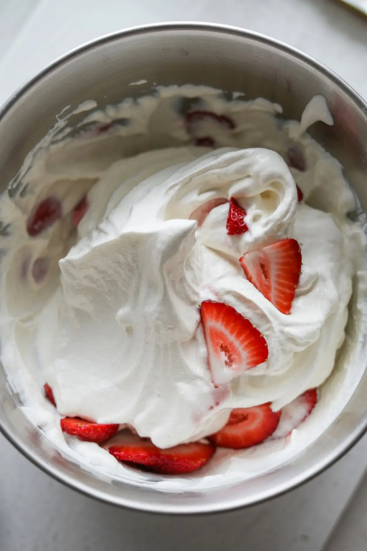 Freshly whipped cream mixed with sliced strawberries in a stainless steel bowl, ready for layering into strawberry shortcake or vanilla strawberry cake.