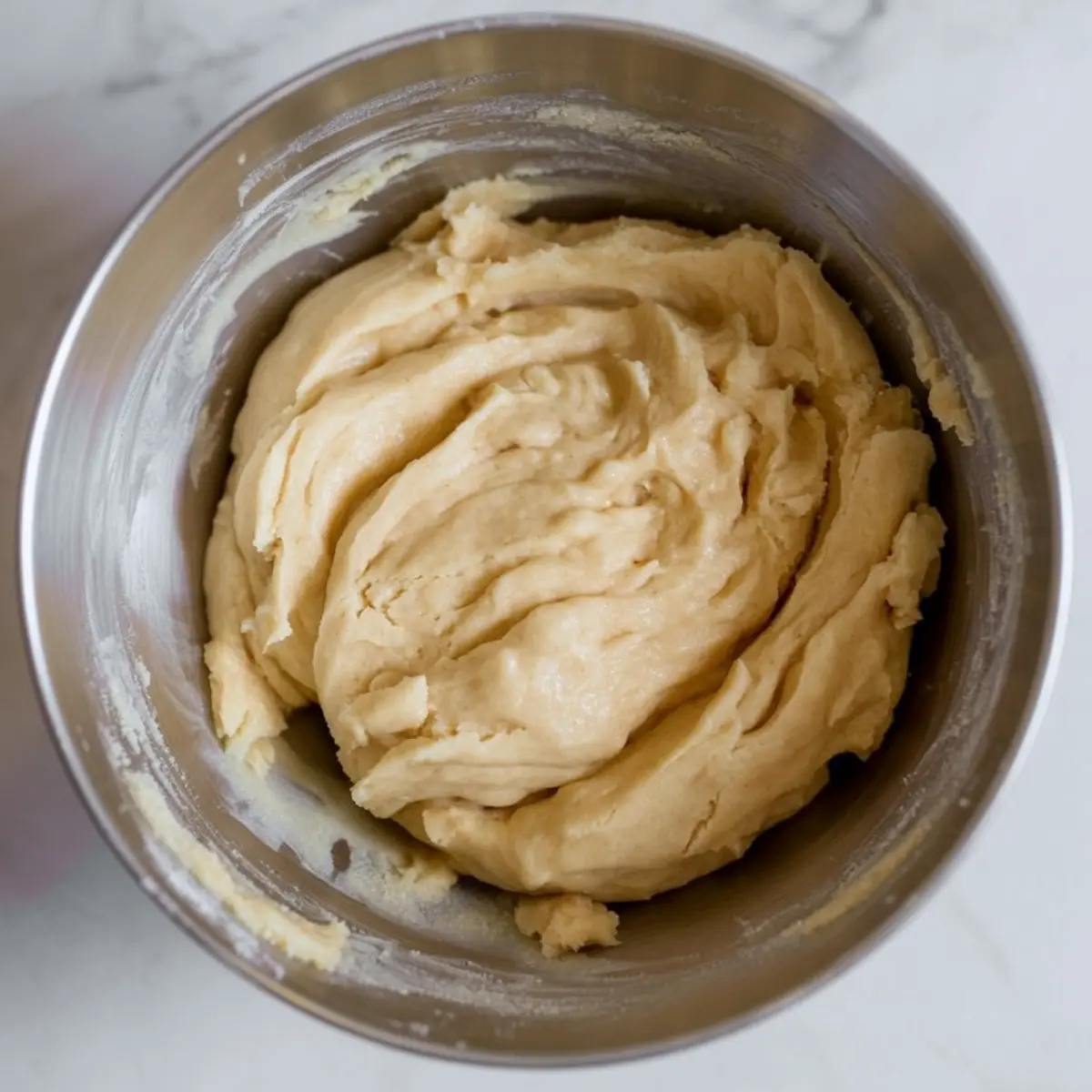 Thick sugar cookie dough in a metal mixing bowl, with a creamy texture perfect for shaping into cookie cups.
