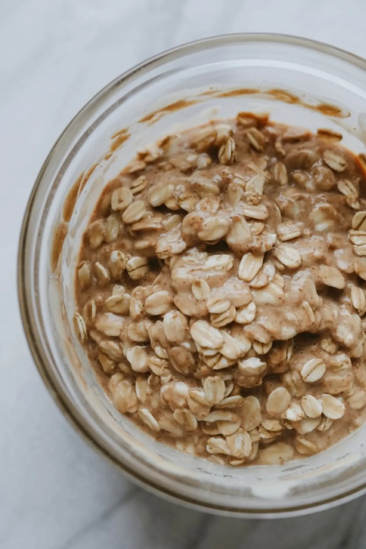 Glass bowl filled with a thick oatmeal and nut butter mixture, showing the textured base layer for tiramisu overnight oats preparation.