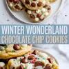 Stacked festive chocolate chip cookies on a white plate, packed with white and semi-sweet chocolate chips, holiday sprinkles, and a soft center shown in a close-up cookie bite.