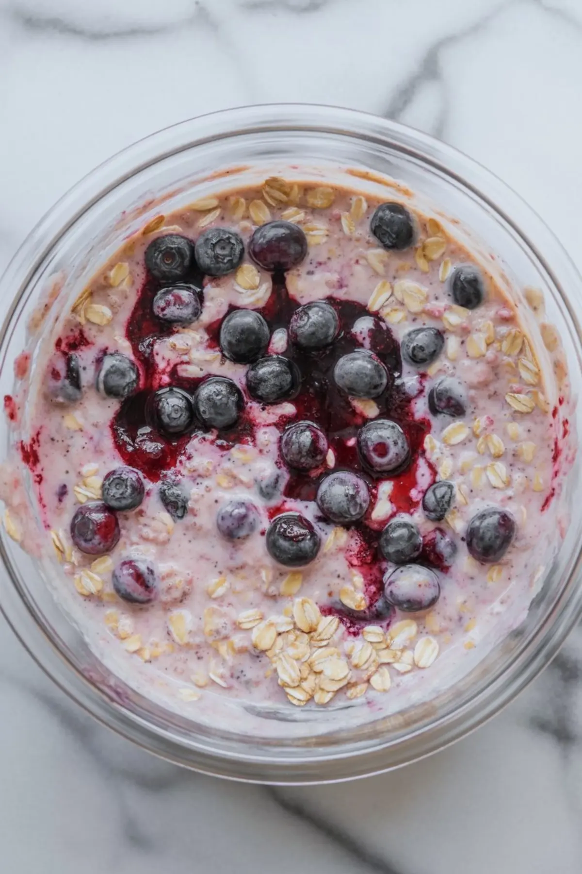 Thick blueberry overnight oats in a glass bowl, topped with fresh blueberries and swirled with vibrant blueberry compote.
