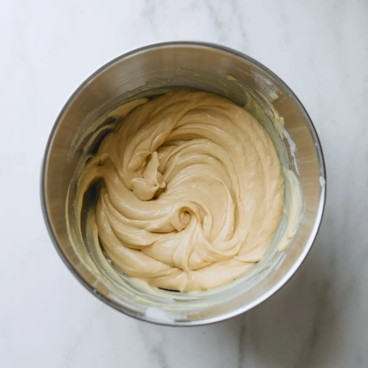 Smooth and glossy cake batter swirled in a metal bowl, fully mixed and ready for baking.