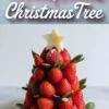 Pinterest pin image featuring a strawberry Christmas tree topped with a pineapple star and dusted with powdered sugar, paired with bold typography that reads “Strawberry Christmas Tree” over a marble background.