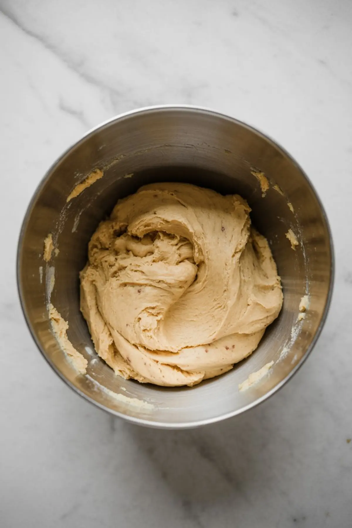 Chilled cookie dough in a stainless steel mixing bowl with a smooth, firm texture.
